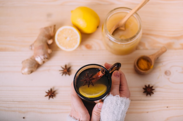 Chiuda su delle mani femminili che tengono la tazza di acqua calda con il limone