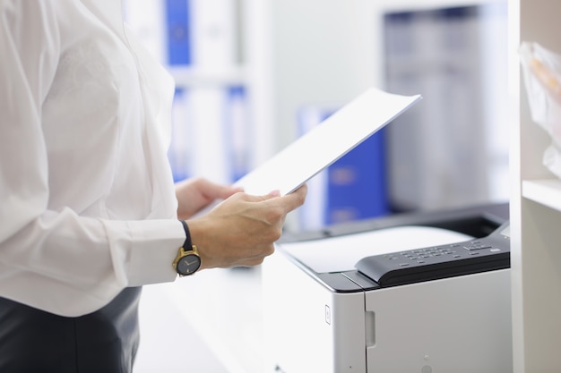Close-up of female hands holding documents. Businesswoman standing near copier in office. Annual report and routine paper work concept. Business and management idea