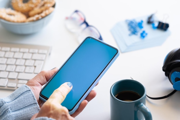 Close-up on female hands holding smart phone with blue display. Blue color on accessories