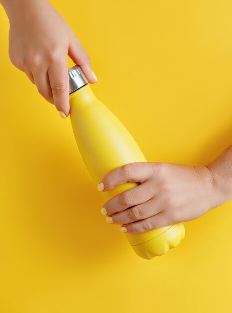 Photo close up of female hands holding yellow reusable steel bottle on yellow background