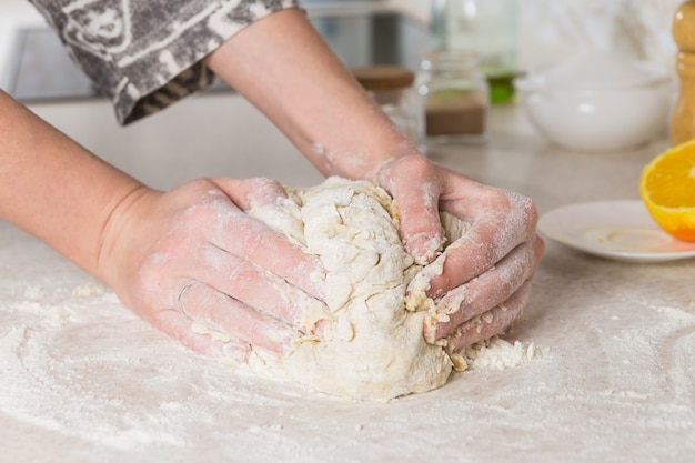 Primo piano delle mani femminili che impastano pasta in cucina minimalista moderna. preparare e mescolare l'impasto.