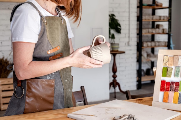 女性の手をクローズアップ粘土から料理を作るエプロンの女性陶芸家スタジオで陶器を作る