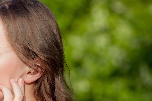 Close-up Of Female Hands Putting Hearing Aid In Ear. Modern digital in the ear hearing aid for deafness and the hard of hearing patients