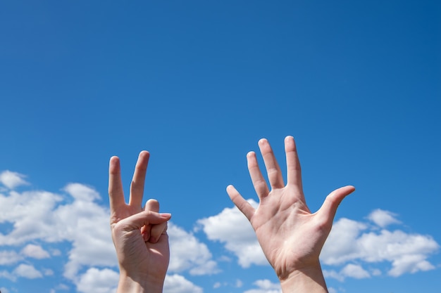 Close-up of female hands showing seven fingers on a blue sky.