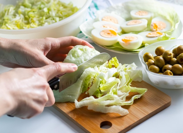 Close up of female hands slicing green salad on wooden board over a white table background