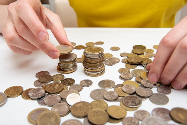 Photo close-up of female hands stack coins in a vertical column, on the table are many coins of different countries.