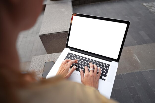 Close up of female hands typing on computer keyboard of a laptop sitting in the street