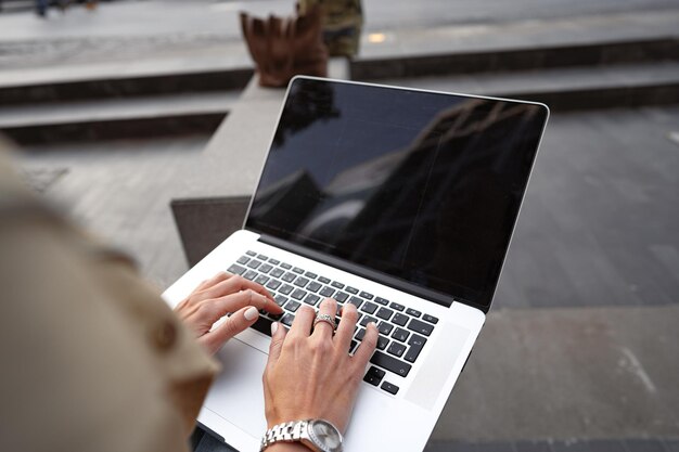 Close up of female hands typing on computer keyboard of a laptop sitting in the street