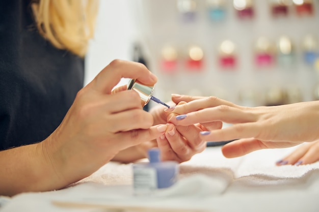 Close up of female hands while beauty professional is painting them with blue gel polish