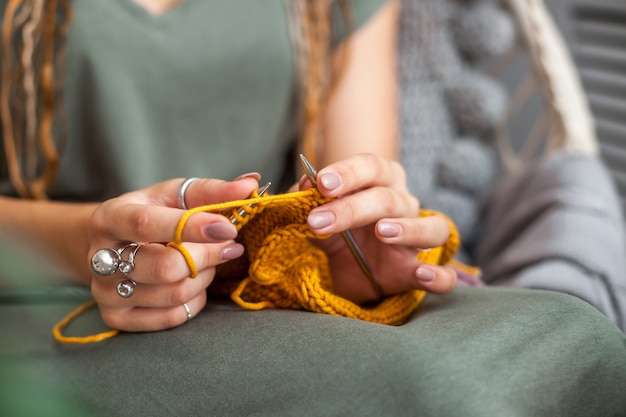 Close-up of female hands with knitting. Metal knitting needles. Yellow knitted fabric.