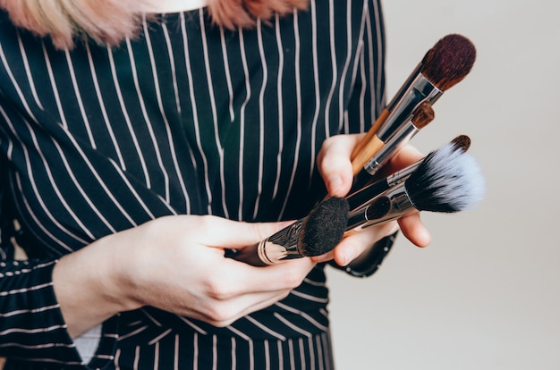 Close-up of female hands with make-up brushes. woman in black dress