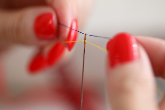 Primo piano della femmina che tiene i fili blu e gialli nell'ago. combinazione colorata. sarta professionista che prepara le cose per il lavoro. nuova collezione. concetto di fabbrica di moda