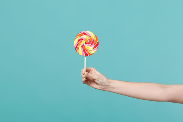 Close up female holding in hand colorful round lollipop isolated on blue turquoise wall background. Proper nutrition or sweets dessert fast food, dieting morning concept. Copy space for advertisement.