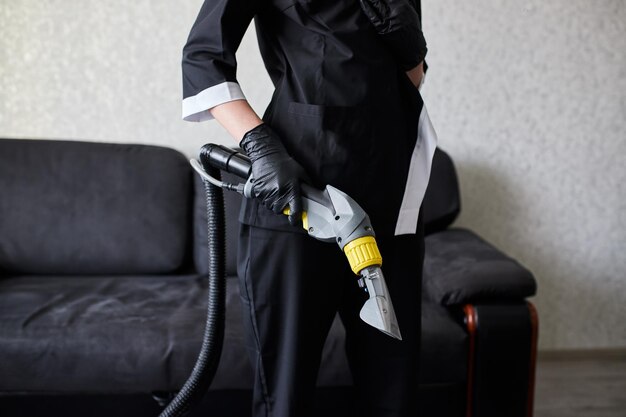 Close up of female housekeeper arm cleaning sofa with washing vacuum cleaner Cleaning service company employee removing dirt from furniture in flat with professional equipment