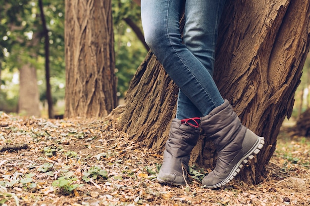 Primo piano delle gambe femminili in jeans e stivali nel parco di autunno