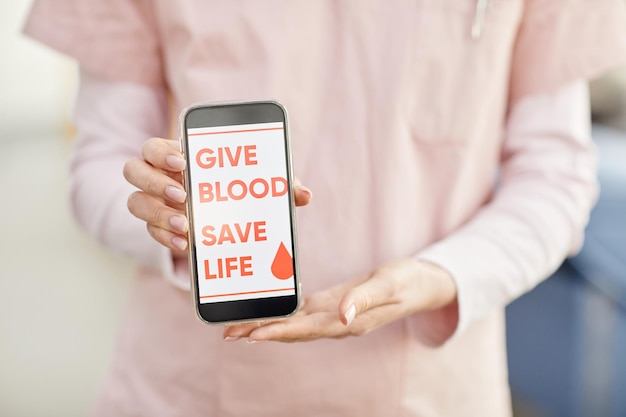 Close up of female nurse holding smartphone with give blood save life slogan at blood donation cente