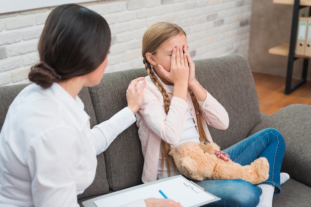 Photo close-up of a female psychologist giving support to the crying girl sitting on sofa with teddy bear