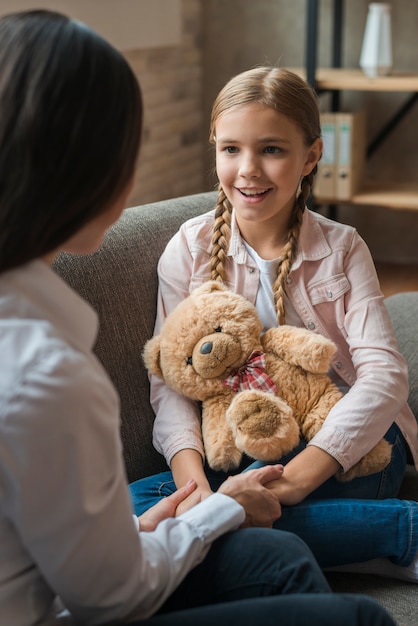 Close-up of female psychologist holding hands of her patient with teddybear
