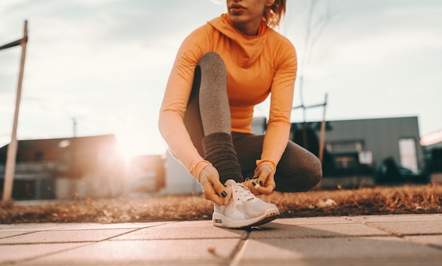 Close up of female runner kneeling and tying shoelace on the street on sunny day