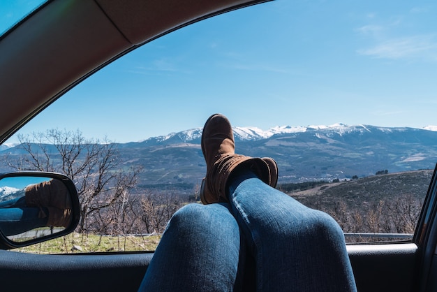 Photo close up of female's feet sticking out of car window with a beautiful view of mountains under a clear sky