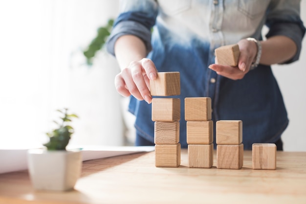 Photo close-up of female's hand stacking wooden block on table at office