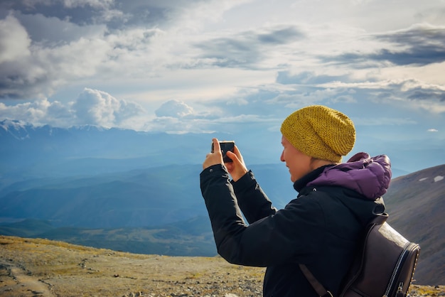 Close up female traveller on top of hill taking picture of beautiful mountain landscape on cloudy sunny day on smartphone Freedom travel concept