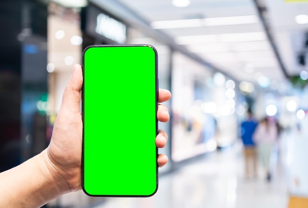 Primo piano di uso femminile smartphone con mano con schermo verde vuoto vuoto immagini sfocate tocco di sfocatura astratta dello sfondo del complesso commerciale interno, concetto di shopping online.