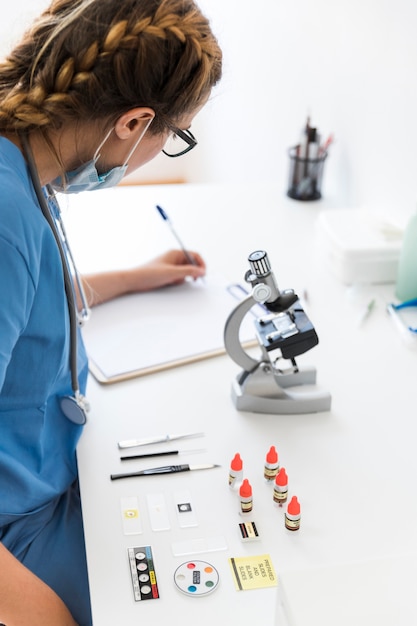 Close-up of female veterinarian writing on clipboard with microscope and medical equipments in laboratory desk