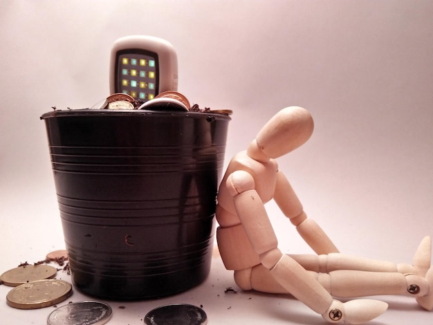 Close-up of figurine by bucket with coins over white background