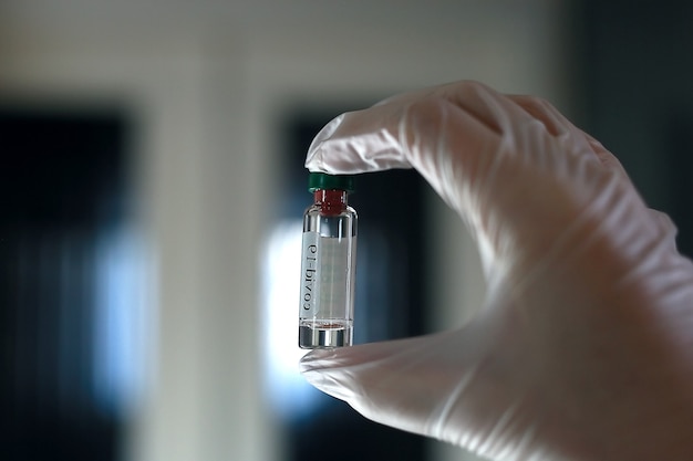 Close-up. The fingers of a hand in a medical glove hold a glass bottle of medicine.