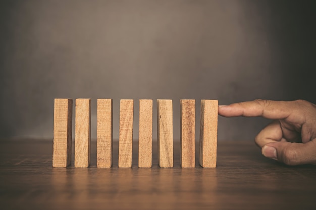 Close-up fingers prevent the wooden block from falling domino.