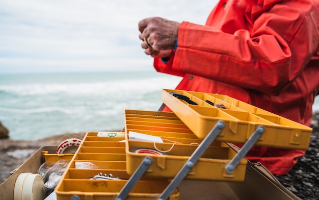 Foto primo piano di un pescatore che mette sull'esca con la scatola dell'attrezzatura di pesca. concetto di pesca e sport.