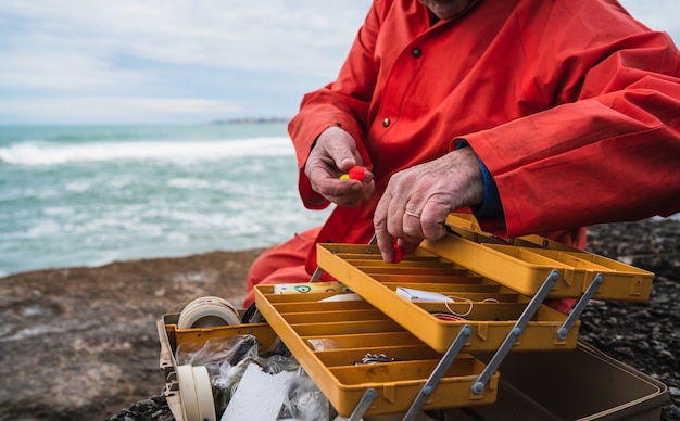 Foto primo piano di un pescatore che mette sull'esca con la scatola dell'attrezzatura di pesca.