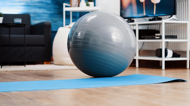 Close up of fitness toning ball used to exercise posture and do physical activity on yoga mat. Nobody in empty space with sport and workout equipment. Living room with training tools.