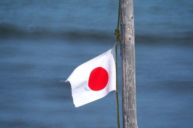 Photo close-up of flag hanging on pole against sea