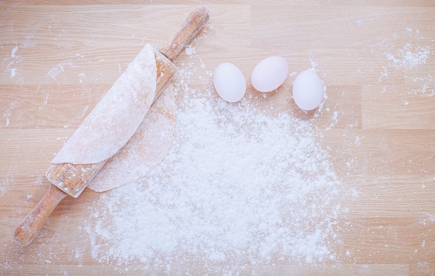 Close up of flat lay of flour, dough and eggs on wooden panel