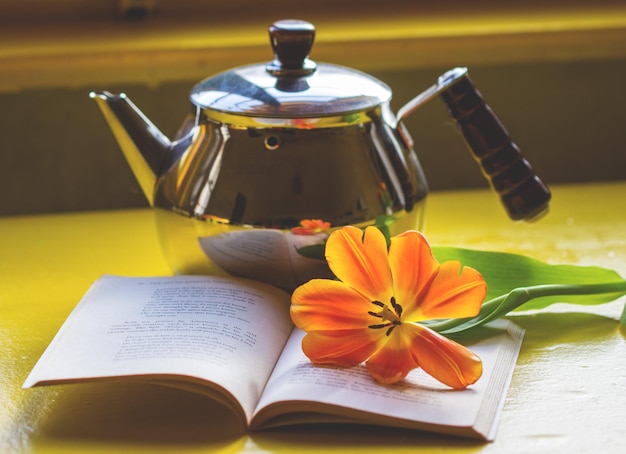 Foto close-up di un fiore su un libro aperto con una teiera sul tavolo