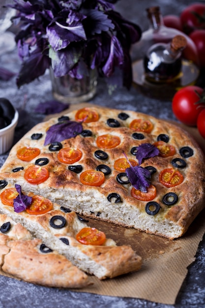 Close up on focaccia with tomatoes, black olives and basil