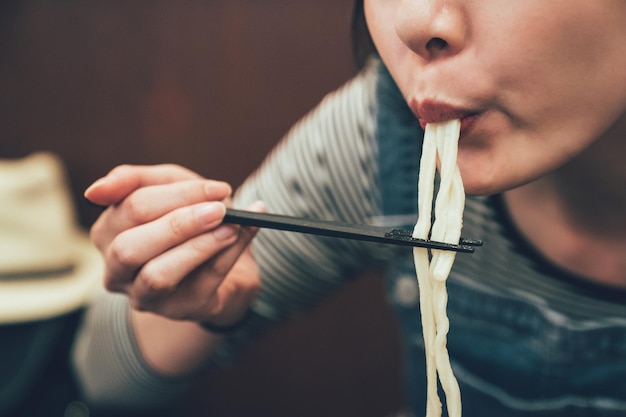 Close-up focus Aziatische vrouw die eetstokjes gebruikt om de noedels in de mond te knippen. jonge vrouwelijke japans eten lunch proeven heerlijke udon ramen in osaka japan. indoor restaurant concept levensstijl.