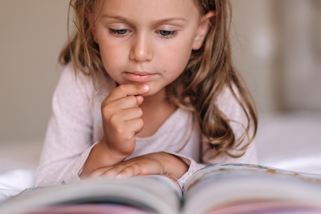 Primo piano ragazza bambino concentrata leggere il libro a lettogiornata internazionale dell'alfabetizzazione