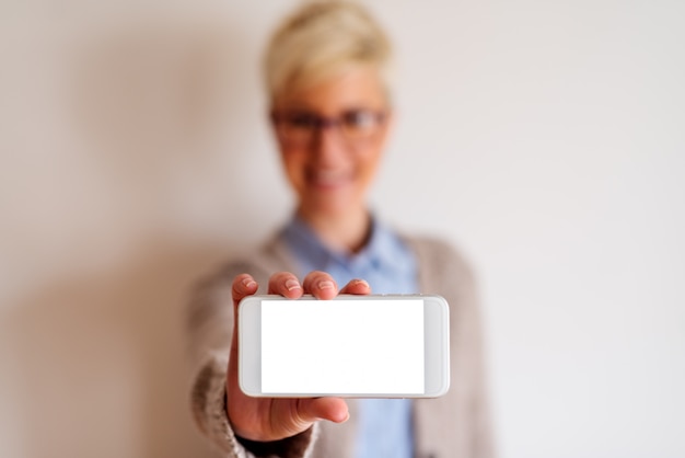 Close up of a focused view of a white cell phone with white screen . Blurred picture of a girl behind the telephone holding it.
