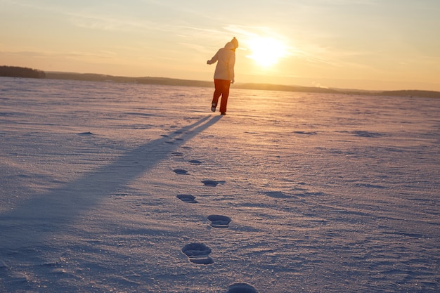 Close-up footprints in the snow. The girl leaves towards the sunset.