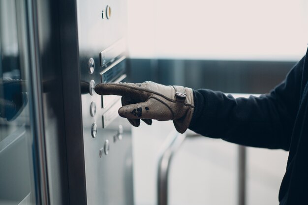 Крупным планом указательный палец в перчатке, нажимающий кнопку лифта во время концепции карантина пандемии коронавируса covid-19