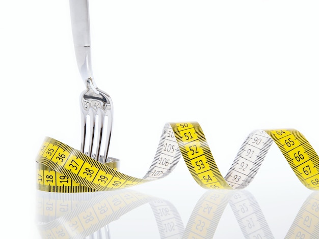 Close-up of fork and tape measure on white background