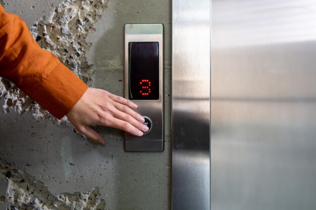 Close-up foto de hand van een jonge vrouw in een oranje shirt die met haar op een metalen liftknop drukt