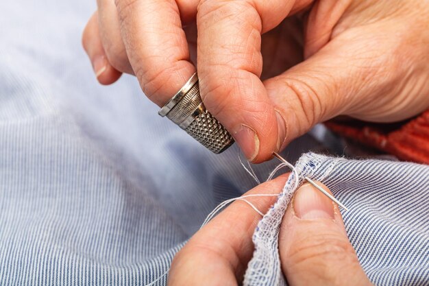 Foto close-up foto extreme horizontale handen volwassen blanke vrouw die met naald en steek naait om een blauw shirt te repareren die het handwerk van een kleermaker doet