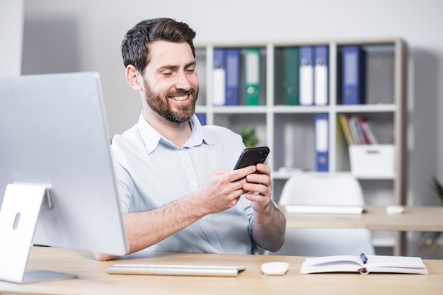 Close-up foto Gelukkige en vrolijke kantoormedewerker directeur met een mobiele telefoon Kreeg het goede nieuwsbericht Zittend op kantoor aan een computerbureau