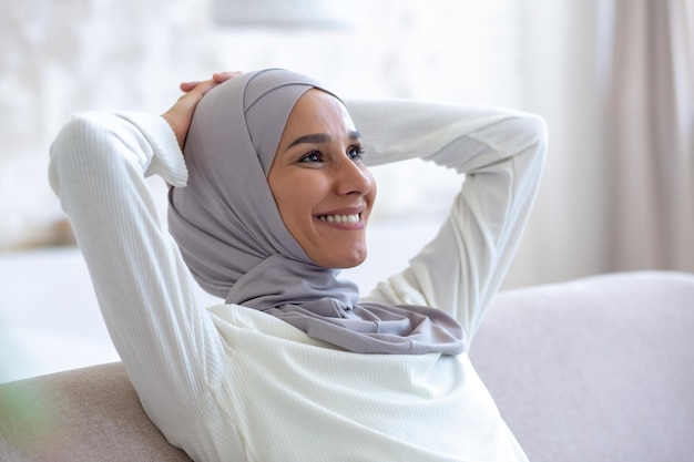 Close-up foto lachende Arabische jonge zakenvrouw in hijab zittend op de bank thuis met de handen achter