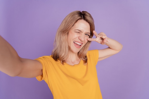 Close-up foto mooie vrouw gelukkig positieve glimlach maken selfies wink eye show vrede cool v-teken geïsoleerd over paarse kleur achtergrond