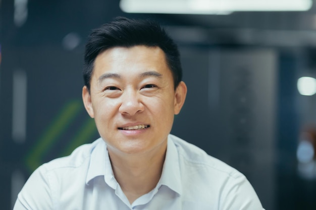 Close-up foto portret van jonge knappe lachende Aziatische zakenman in wit overhemd in moderne kantoor